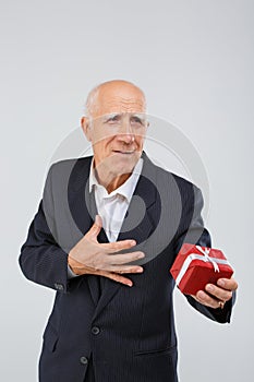 Portrait of an elderly man on a white background, in the studio, in a smart suit with a red gift box in his hand.