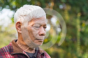 Portrait of an elderly man worried and looking down while standing in a garden. Space for text. Concept of aged people