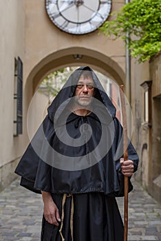 Portrait of an elderly monk 45-50 years old with a beard and a black cassock, walking down the street with a staff against the bac