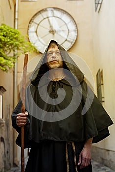 Portrait of an elderly monk 45-50 years old with a beard and a black cassock, walking down the street with a staff against the bac