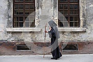 Portrait of an elderly monk 45-50 years old with a beard and a black cassock, walking down the street with a staff against the bac