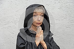 Portrait of an elderly nun 60-65 years old in a black cassock on the light background of the wall.