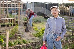 Portrait of an elderly satisfied woman with watering can for watering plants in garden