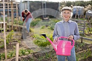 Portrait of an elderly satisfied woman with watering can for watering plants in garden