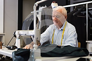 Portrait of elderly tailor working on sewing machine at studio