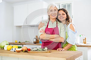 Portrait of elderly woman and her daughter-in-law in an apron in the kitchen - cooking dinner together