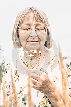 Portrait of an elderly woman holding a bouquet of flowers, smelling the scent of daisies. Autumn