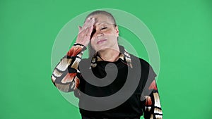 Portrait elderly woman looking at the camera and making a facepalm gesture. Brunette granny in black dress on green
