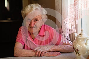 Portrait of an elderly woman pensioner sitting at a table in the kitchen in his house.