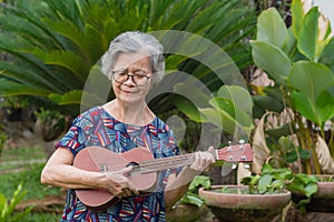 Portrait of an elderly woman playing ukulele while standing in garden