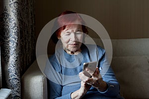 Portrait of elderly woman with smartphone in hands. Old lady with red hair uses smartphone, touches screen of mobile phone with