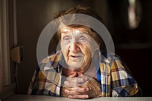 A portrait of an elderly woman in someone else`s shirt slung over her shoulders, in her own home.