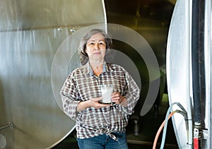 Portrait of a elderly woman standing in the dairy farm, holding a glass of milk