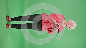 Portrait elderly woman texting on her smartphone. Gray haired grandmother in red blouse on green screen at studio. Slow