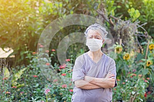 A portrait of an elderly woman wearing a face mask and arms crossed while standing in a garden. Mask for protect virus