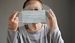 Portrait of an elderly woman wearing a protective medical mask, looking at the camera, on a gray background. Flu epidemic, dust