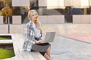 Portrait of elegant confident beautiful businesswoman sitting on bench and typing on laptop. freelance