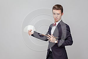 Portrait of elegant magician holding magic wand and pointing at playing cards in his hands. white