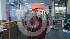 Portrait of elegant slim beautiful woman in hard hat posing in hardware store indoors. Charming brunette Caucasian buyer