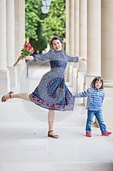 Portrait of elegant woman in a blue dress posing with her sun next to a city building with columns