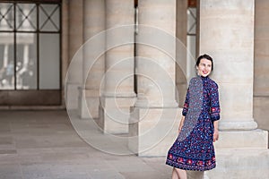 Portrait of elegant woman in a blue dress posing next to a city building with columns