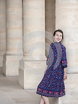 Portrait of elegant woman in a blue dress posing next to a city building with columns