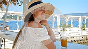 Portrait of elegant woman in straw hat relaxing in beach club bar and looking at the sea view