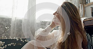 Portrait of elegant woman wearing vintage bridal dress sitting on floor, posing at home in stylish vintage interior