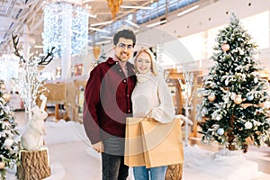 Portrait of elegant young couple enjoying shopping together, holding bags with gifts and looking at camera standing