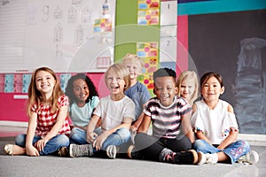 Portrait Of Elementary School Pupils Sitting On Floor In Classroom