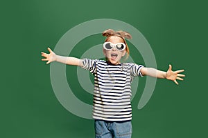 Portrait of emotiona, beautufl little girl, childin striped shirt and sunglasses posing against green studio background photo