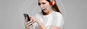 Portrait of emotional beautiful happy plus size model in headphones looking in mobile phone listening to music