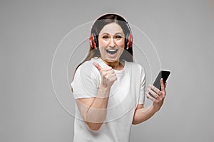 Portrait of emotional beautiful happy plus size model in headphones looking in mobile phone with thumb up listening to