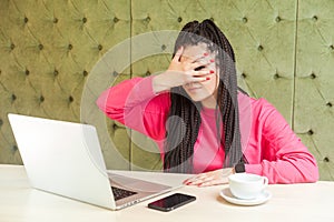 Portrait of emotional disbelief young woman with black dreadlocks hairstyle in pink blouse are sitting in cafe and covering the