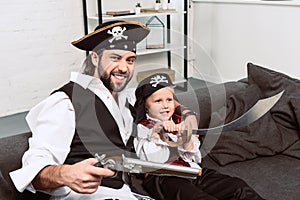 portrait of emotional father and son in pirates halloween costumes sitting on sofa