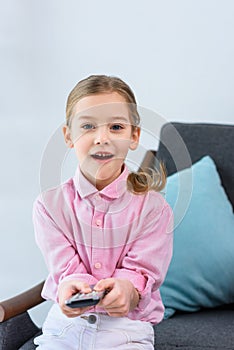 portrait of emotional kid with remote control sitting on sofa