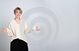 Portrait of emotional woman. Confident woman showing direction with hand on light gray background. Looking at camera