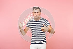 Portrait of emotional young man in striped t-shirt hold wooden word Love isolated on trending pastel pink background