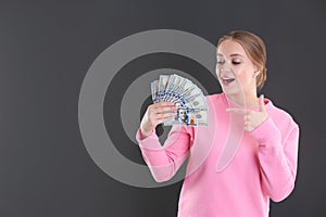 Portrait of emotional young woman with money on grey background