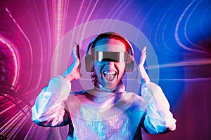 Portrait of emotionally shouting woman in futuristic sunglasses and headphones in pink and blue neon light. Music lover