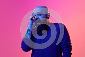 Portrait of emotive bald bearded man in his 30s expressing shocked face, emotions against pink background in neon light