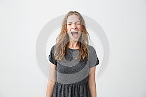 Portrait of emotive young beautiful girl shouting with closed eyes over white background.