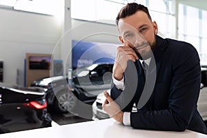 portrait of an employee of a car dealership in the showroom against the background of new cars