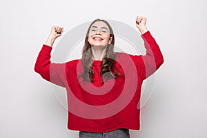 Portrait of energetic woman clenches fists with happiness, has toothy smile, dressed casual red sweater, girl win lottery,