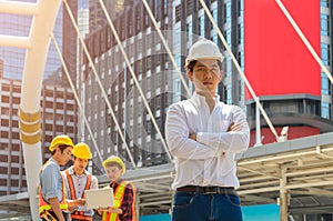 Portrait of engineer or architect in white shirt and safety hat standing in front of the building with group of construction