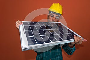 Portrait of an engineer or solar worker in protective work clothes holding photovoltaic panel isolated on orange background