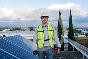 portrait of an engineer standing between solar panels, young adult professional technician electrician looking at camera with
