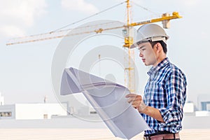 Portrait of engineer wear white safety helmet and verify the blueprint with commitment at construction site with crane background
