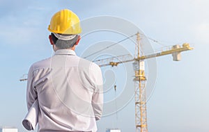 Portrait of engineer wear yellow helmet safety and holding the blueprint at construction site with crane background