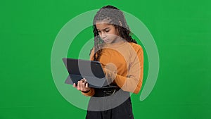 Portrait of engrossed teenage African American girl surfing Internet on tablet thinking on green screen. Absorbed device